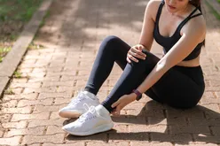 Person sitting on a brick path holding their leg wearing workout attire and sneakers