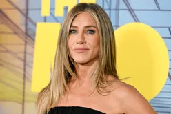 Jennifer Aniston smiling at an event with a backdrop featuring text and graphic design
