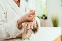 A person in a bathrobe applying cream to their hand blurred background suggesting a relaxing setting