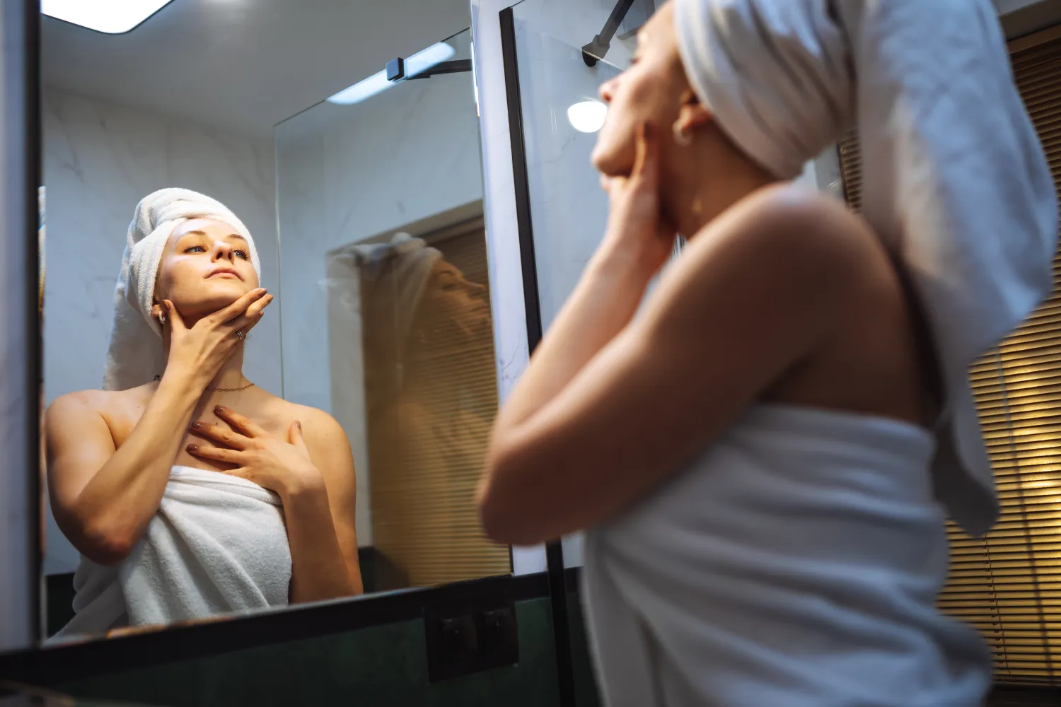 Person with a towel wrapped around her head and body looks up while in front of the mirror.
