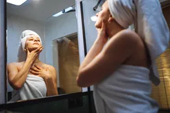 Person with a towel wrapped around her head and body looks up while in front of the mirror.