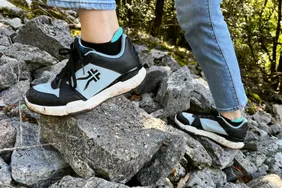 A person wears the Kuru Quantum Sneaker while climbing over rocks